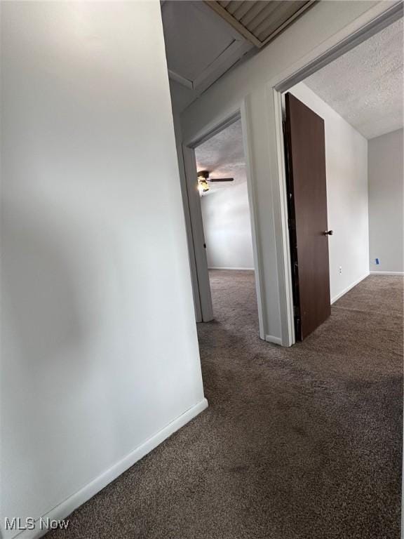 hall featuring dark colored carpet, a textured ceiling, and baseboards