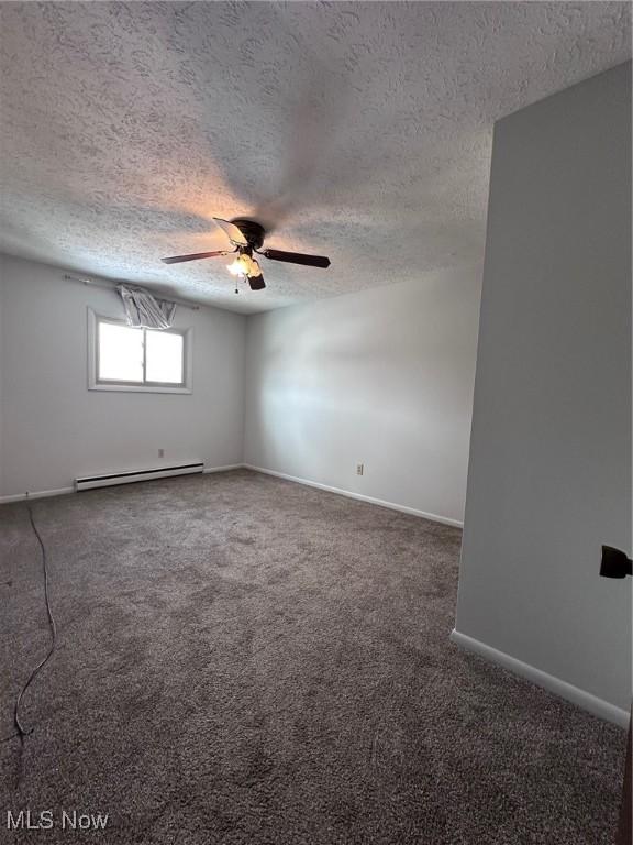 empty room with a textured ceiling, dark colored carpet, baseboard heating, and baseboards