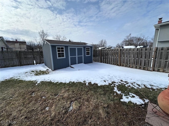 yard covered in snow with a fenced backyard, an outdoor structure, and a storage unit