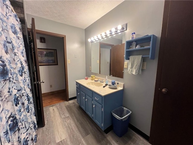 bathroom with a textured ceiling, wood finished floors, vanity, and baseboards