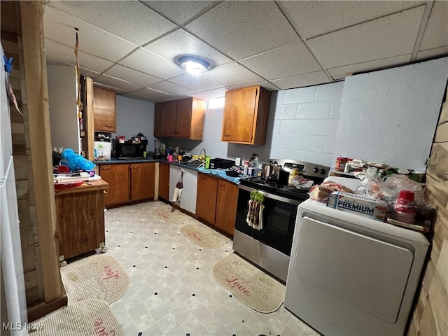 kitchen with concrete block wall, light floors, dark countertops, washer / dryer, and stainless steel range with electric stovetop