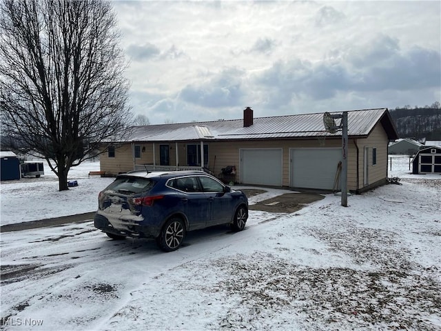 single story home featuring a garage, metal roof, and a chimney