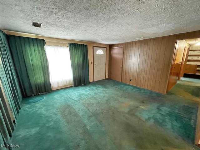 carpeted empty room featuring visible vents, wooden walls, and a textured ceiling