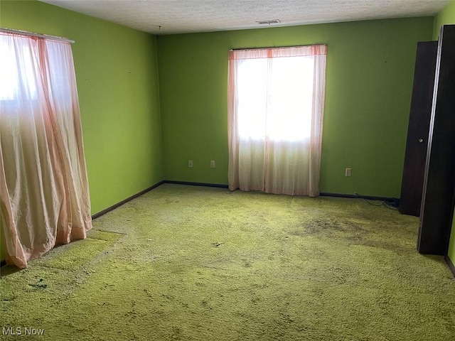 unfurnished room with baseboards, visible vents, a textured ceiling, and carpet flooring