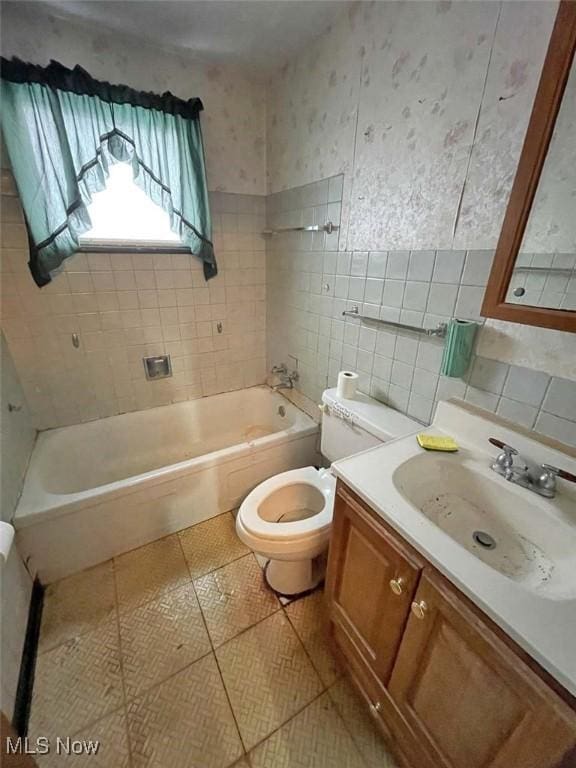 bathroom with wallpapered walls, toilet, tile patterned flooring, vanity, and tile walls