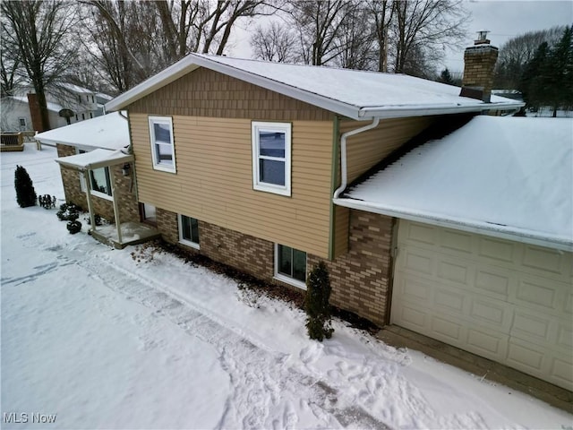 view of snow covered exterior featuring a garage, brick siding, and a chimney