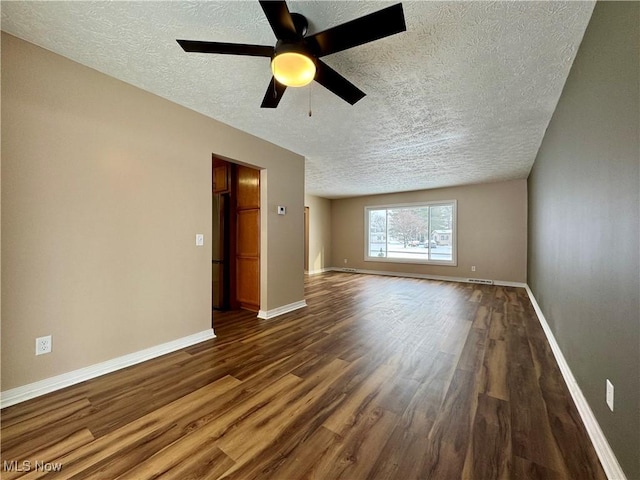 empty room featuring a textured ceiling, ceiling fan, visible vents, baseboards, and dark wood finished floors