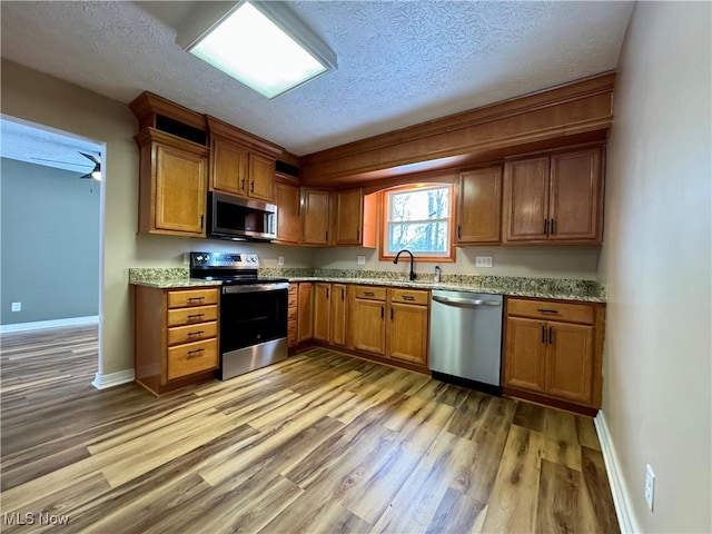 kitchen with a textured ceiling, a sink, light wood-style floors, appliances with stainless steel finishes, and brown cabinetry