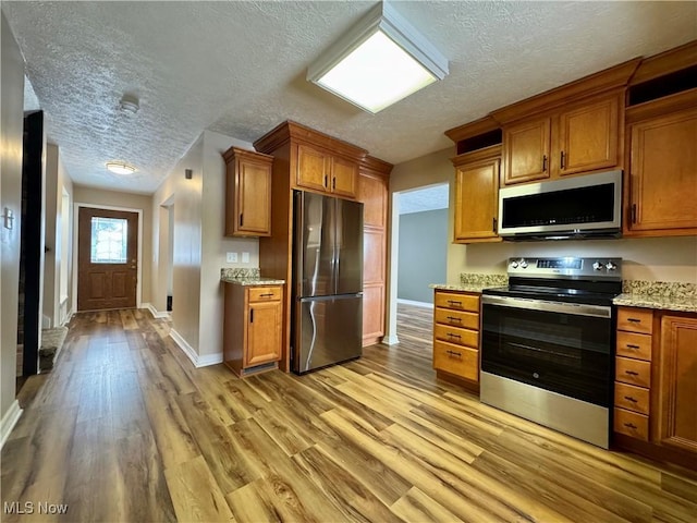 kitchen featuring light wood-type flooring, brown cabinetry, stainless steel appliances, and light stone countertops