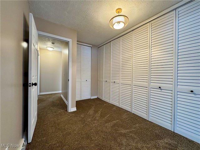 unfurnished bedroom with dark colored carpet, a closet, a textured ceiling, and baseboards