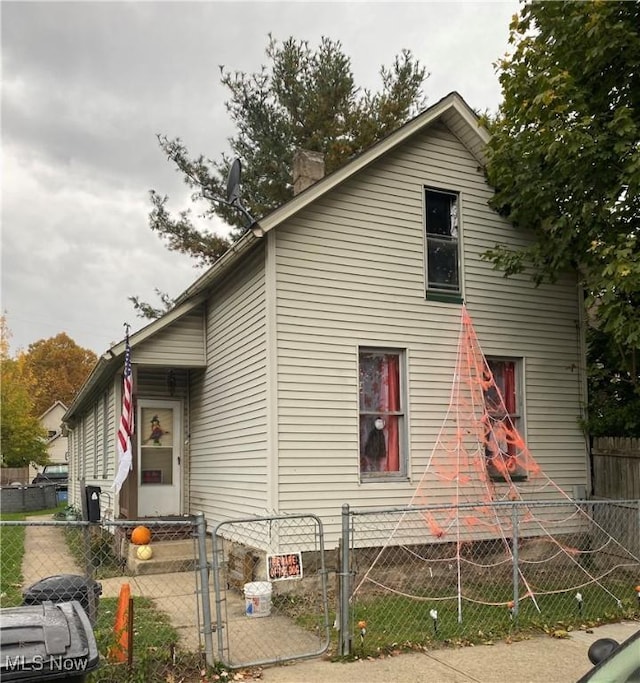 view of side of home with a chimney, fence, and a gate