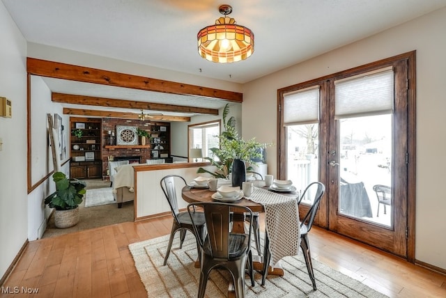 dining room with light wood-style floors, french doors, a fireplace, and beamed ceiling