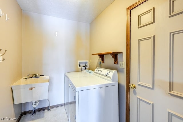 laundry area featuring a textured ceiling, laundry area, a sink, baseboards, and washer and clothes dryer