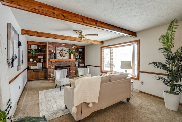 living area with light colored carpet, wainscoting, a textured ceiling, a brick fireplace, and beam ceiling