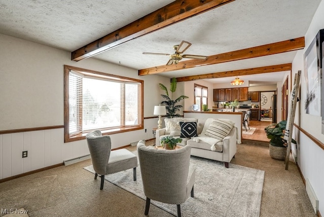 living room featuring a textured ceiling, beamed ceiling, light carpet, and a wainscoted wall