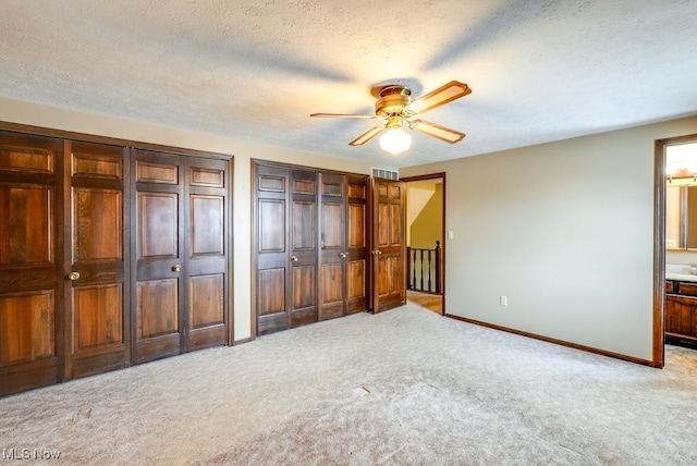 unfurnished bedroom featuring light carpet, a textured ceiling, two closets, and baseboards