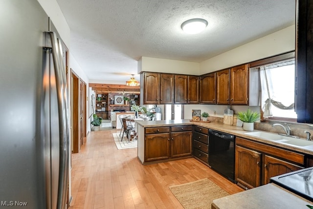 kitchen featuring black dishwasher, light countertops, freestanding refrigerator, a sink, and a peninsula