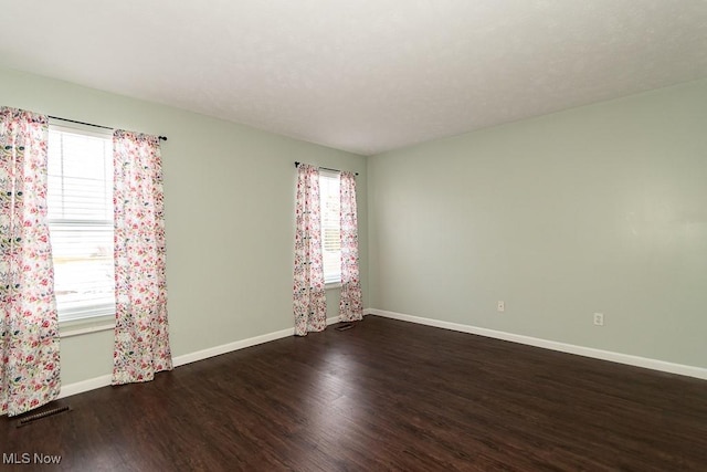 spare room with dark wood-type flooring and plenty of natural light