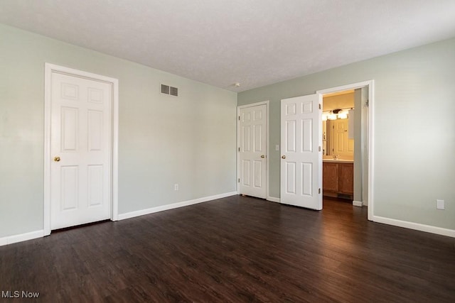 unfurnished bedroom featuring connected bathroom, dark wood finished floors, visible vents, and baseboards