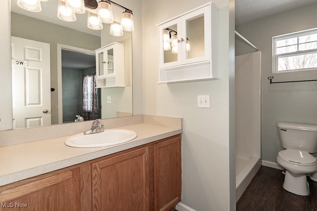 full bath with toilet, a stall shower, vanity, wood finished floors, and baseboards