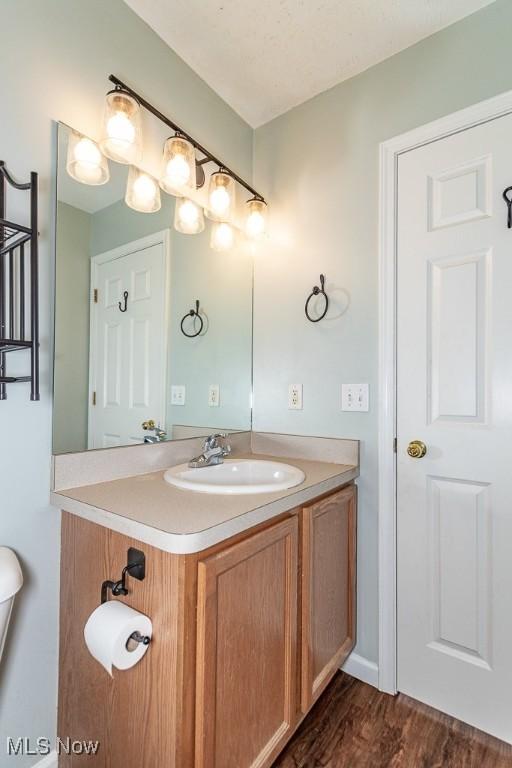 half bath with toilet, wood finished floors, and vanity