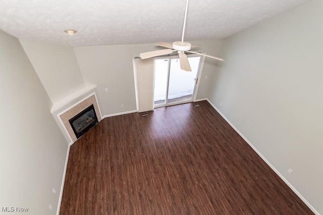 unfurnished living room with ceiling fan, a tiled fireplace, baseboards, and dark wood-type flooring