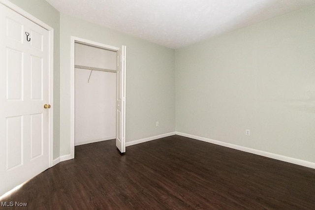 unfurnished bedroom with a closet, baseboards, and dark wood-style flooring