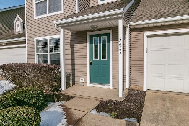 entrance to property featuring a shingled roof and an attached garage