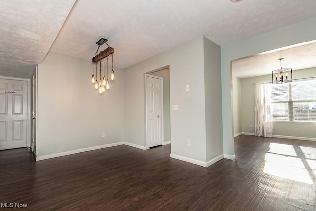spare room with dark wood-style flooring, baseboards, and an inviting chandelier