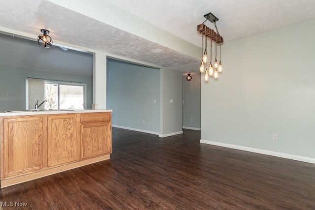 kitchen featuring dark wood-type flooring, a sink, baseboards, and pendant lighting
