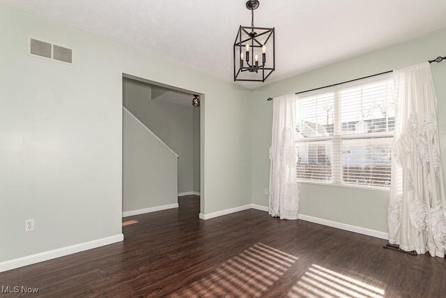 empty room with a chandelier, baseboards, visible vents, and dark wood-style floors