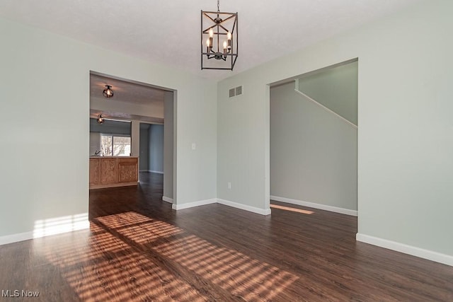 spare room with a notable chandelier, dark wood finished floors, visible vents, and baseboards