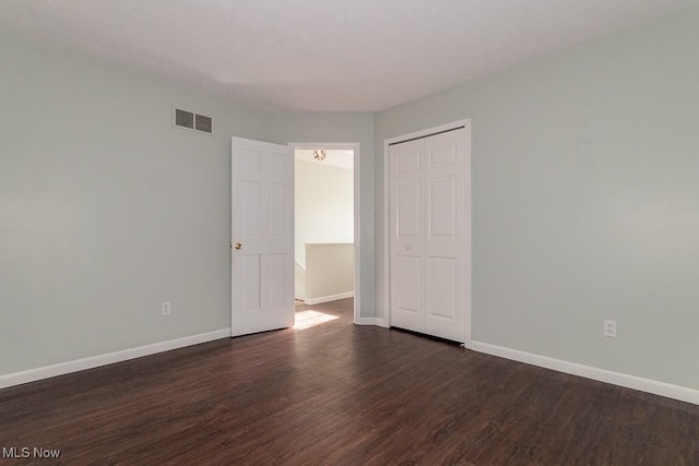 unfurnished bedroom with baseboards, visible vents, dark wood finished floors, and a closet