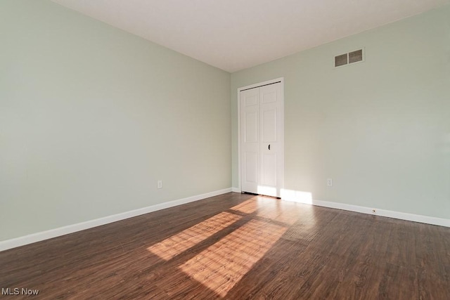 empty room with dark wood-style flooring, visible vents, and baseboards