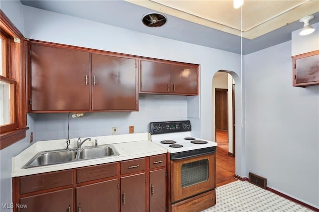 kitchen featuring arched walkways, range with electric cooktop, a sink, light countertops, and tasteful backsplash