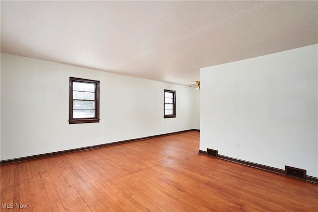 empty room with light wood finished floors, baseboards, visible vents, and a ceiling fan