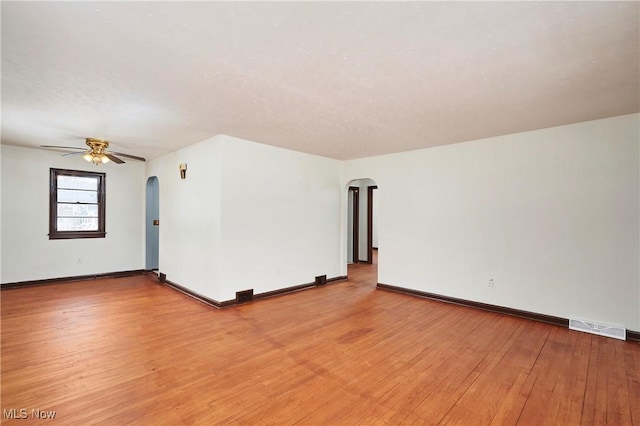 empty room with light wood-style floors, arched walkways, visible vents, and baseboards