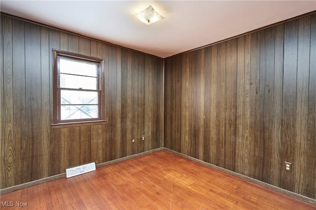 unfurnished room featuring light wood-style flooring, wood walls, visible vents, and baseboards