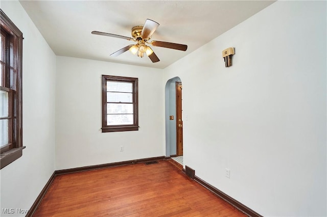 unfurnished room featuring baseboards, ceiling fan, arched walkways, and wood finished floors