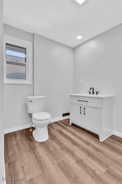 half bath featuring toilet, wood finished floors, vanity, and baseboards