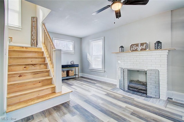 living area with baseboards, a ceiling fan, stairway, light wood-style floors, and a fireplace