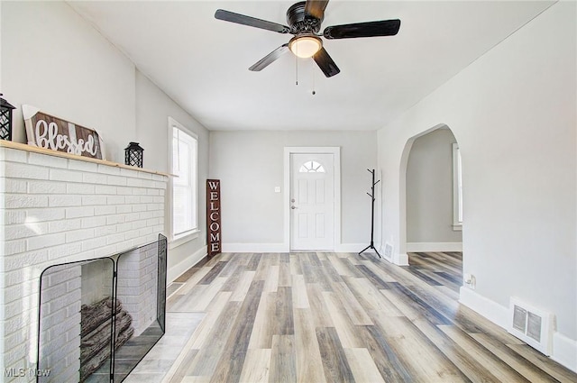 unfurnished living room featuring baseboards, visible vents, arched walkways, light wood-type flooring, and a fireplace