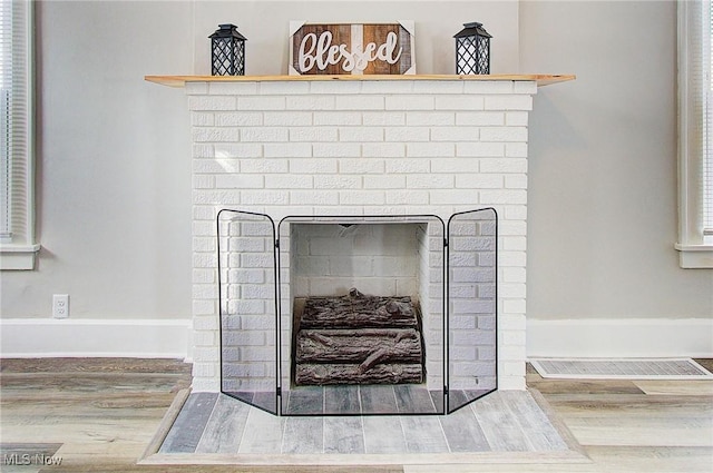 room details with a brick fireplace, visible vents, baseboards, and wood finished floors