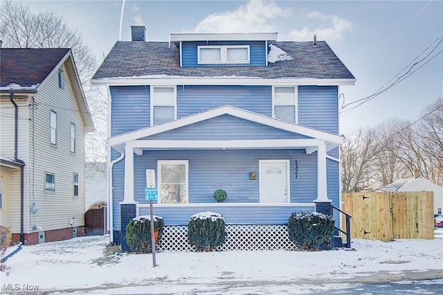 american foursquare style home with covered porch, a chimney, and fence