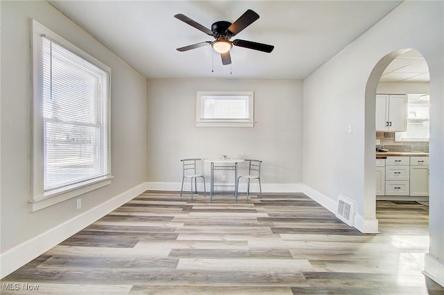 spare room featuring arched walkways, light wood-type flooring, visible vents, and baseboards