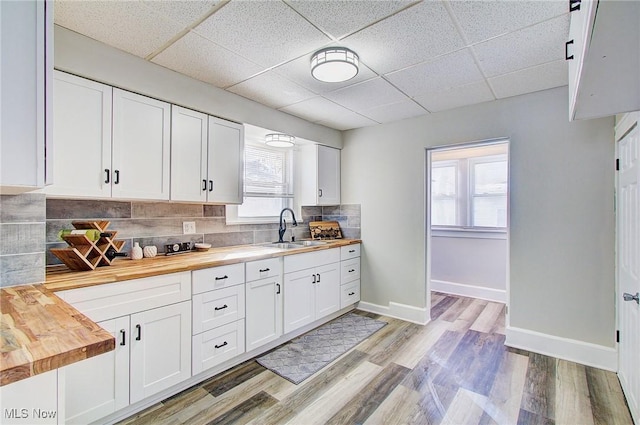 kitchen featuring butcher block countertops, white cabinets, a sink, and backsplash