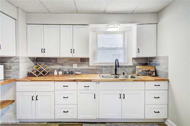 kitchen featuring tasteful backsplash, butcher block counters, white cabinets, and a sink