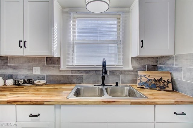 kitchen with decorative backsplash, a sink, wood counters, and white cabinets