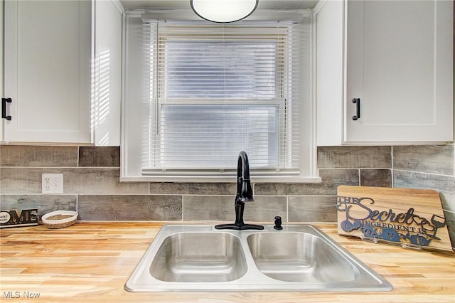 kitchen with wooden counters, a wealth of natural light, a sink, and white cabinetry