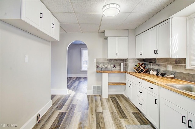 kitchen featuring butcher block counters, visible vents, white cabinets, and arched walkways